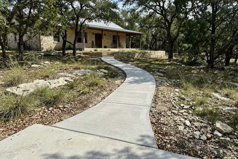 Curving concrete walkway across a rocky yard to a stone house