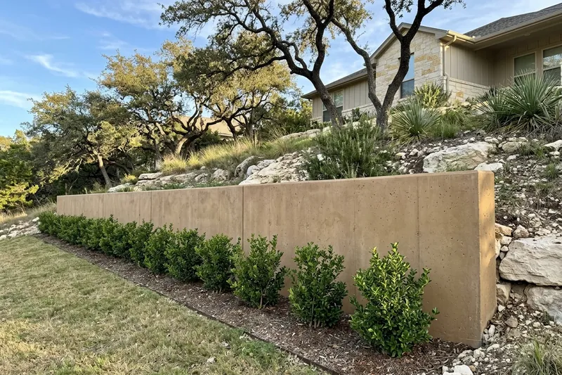 Tan-colored concrete retaining wall with shrubs planted along its base