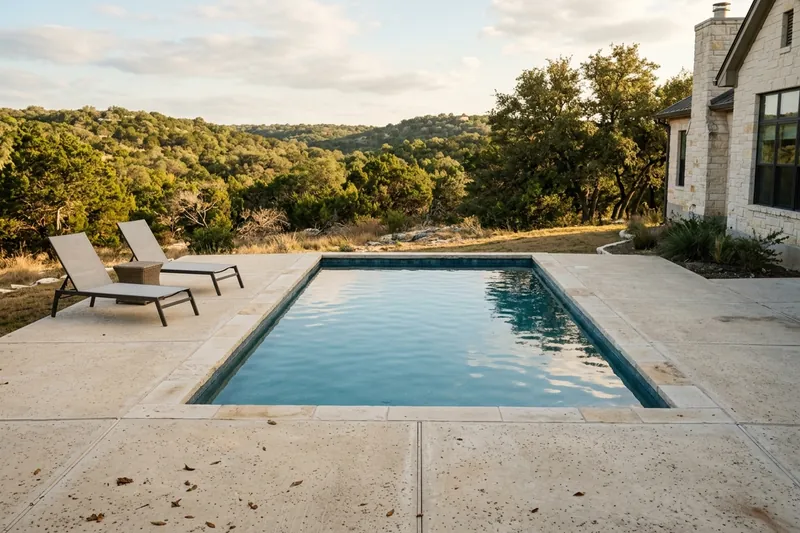 Light concrete pool deck with stone coping at a hillside home