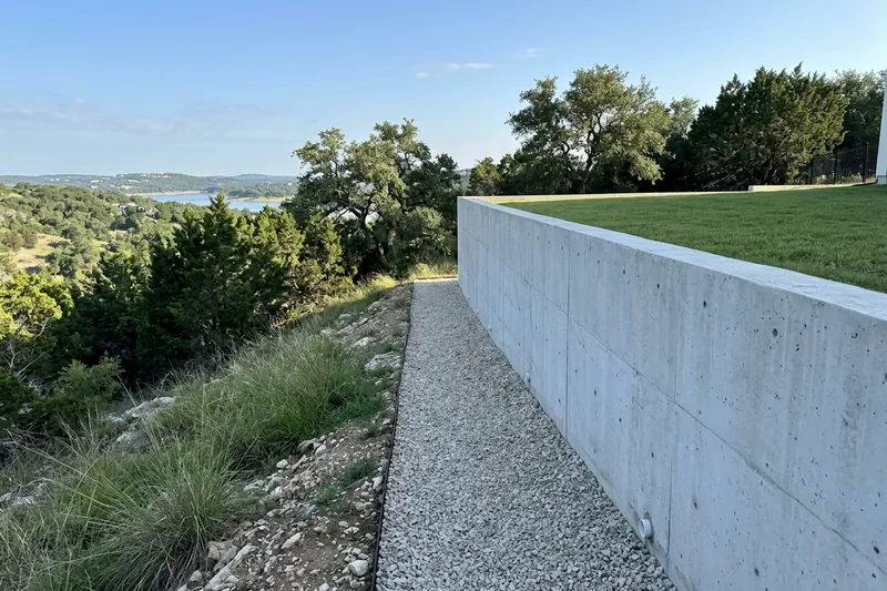 Poured concrete wall terracing a steep backyard above wooded hills