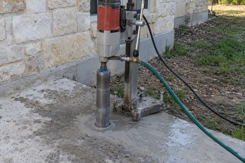 Rig-mounted core drill boring through a slab beside a wall