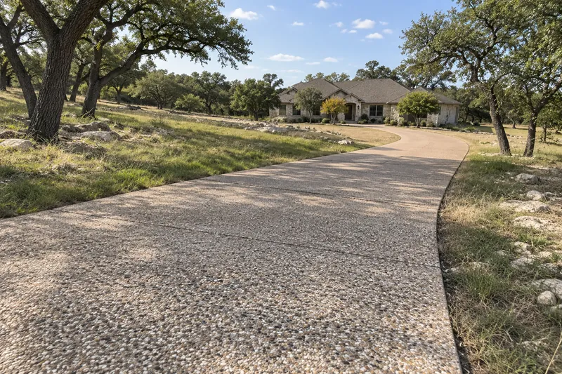 Long exposed-aggregate driveway winding through oak trees