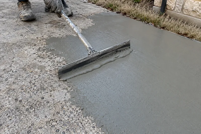 Squeegee spreading a gray resurfacer over worn, pitted concrete